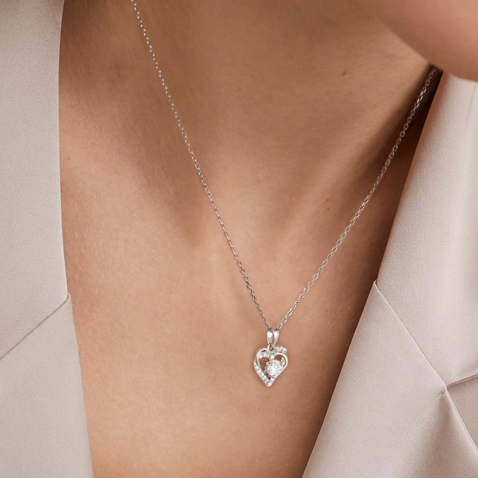 Silver heart-shaped necklace with a pendant on a person wearing a light-colored top.