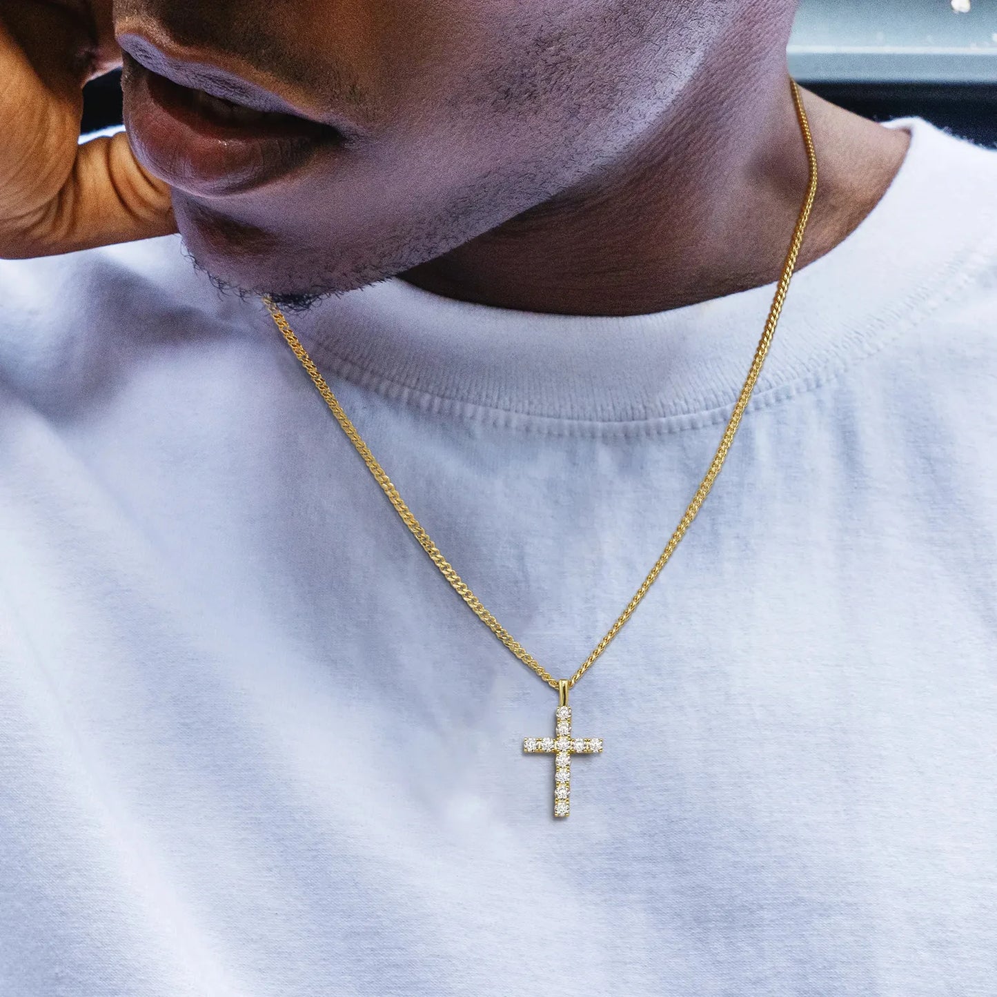 Man wearing a gold cross necklace on a white shirt